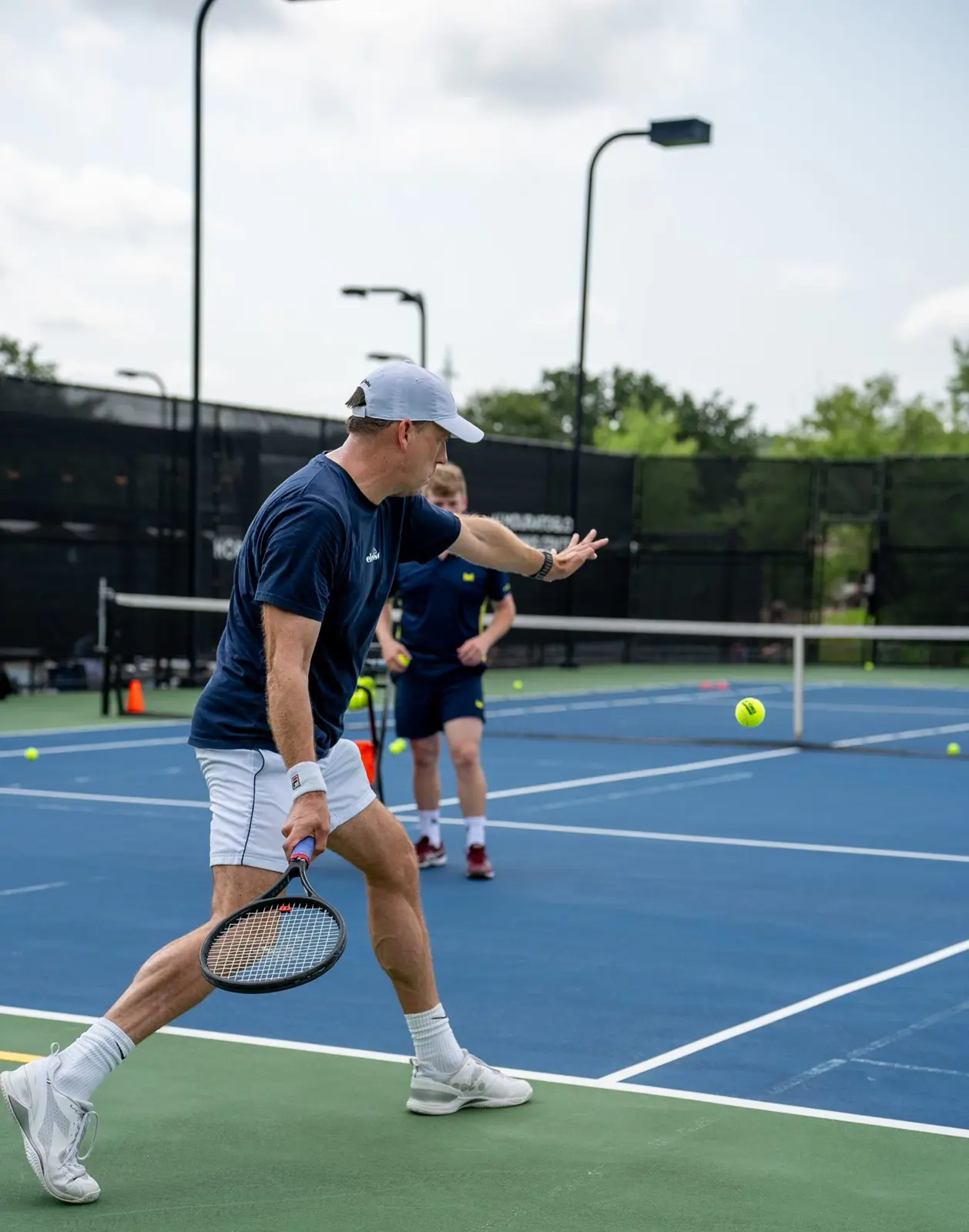 Ein Spieler bereitet eine Vorhand vor, hinter ihm ein Coach