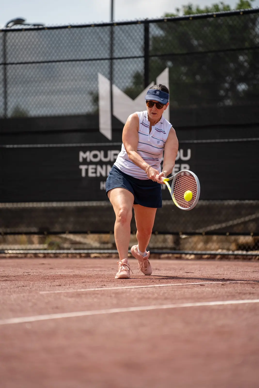 Mujer golpeando un revés en una pista de tierra batida roja del Mouratoglou Tennis Center Horseshoe Bay.