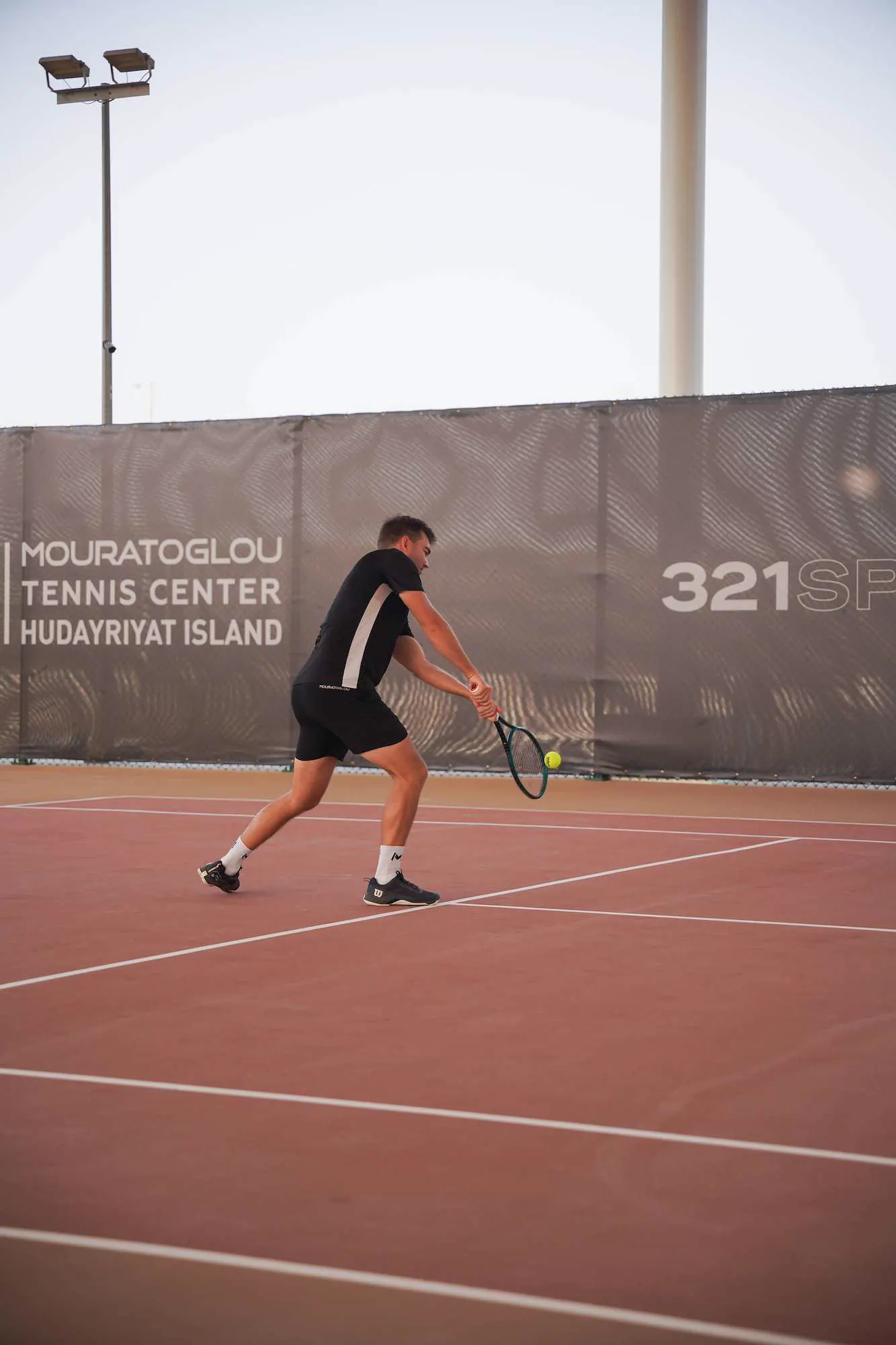 Jugador golpeando un revés frente al muro del Mouratoglou Tennis Center Hudayriyat Island.