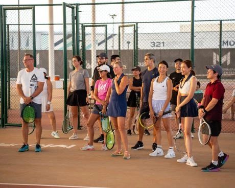Grupo de jugadores adultos escuchando a su entrenador durante una sesión de tenis en el Mouratoglou Tennis Center Hudayriyat Island de Abu Dabi.
