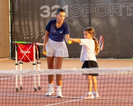 Entrenador Mouratoglou enseñando a una niña en las pistas de tenis de Hudayriyat Island, en Abu Dabi, con atención a la técnica y la confianza.