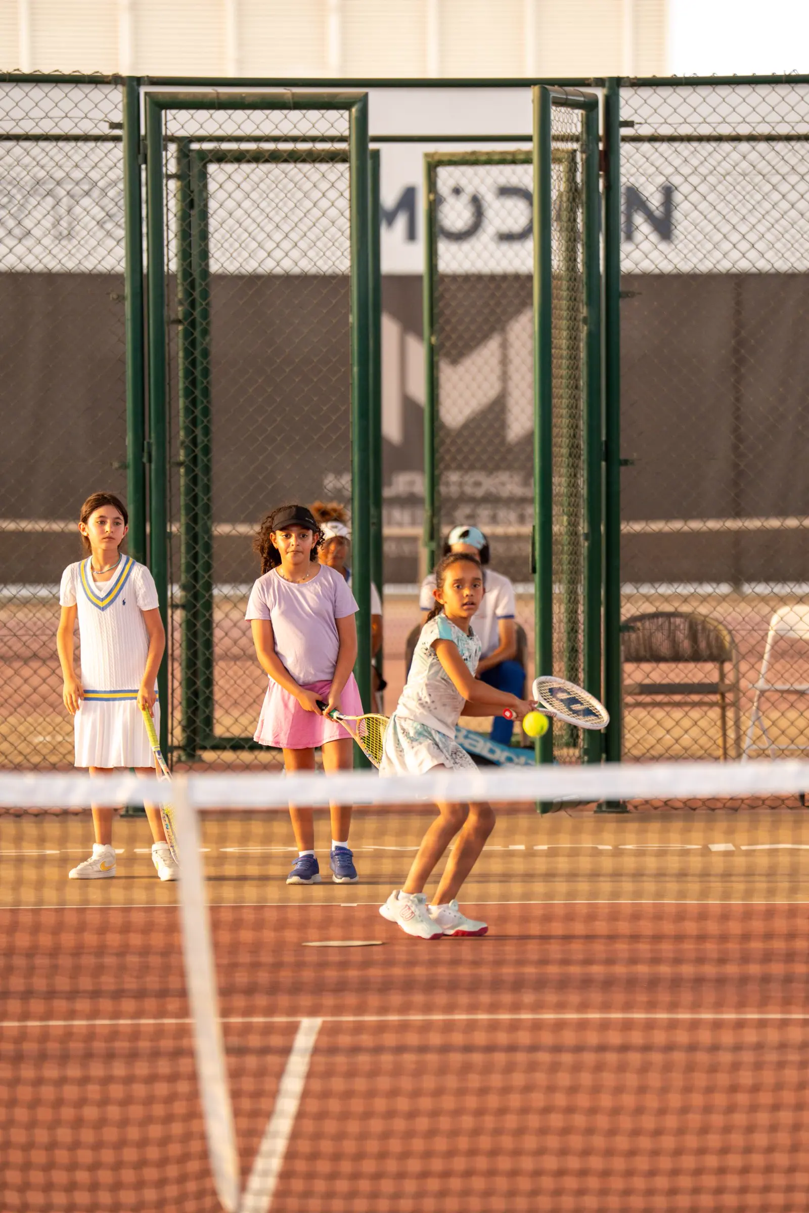 Tre giovani giocatori ricevono una palla dal loro coach durante una sessione junior ad Abu Dhabi