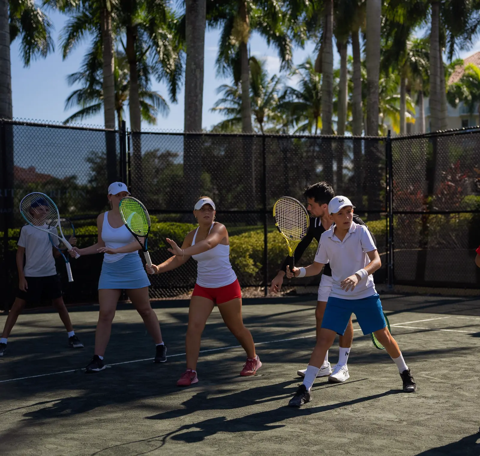 Juniorspieler trainieren gemeinsam mit ihrem Coach auf einem von Palmen gesäumten Platz im Freien