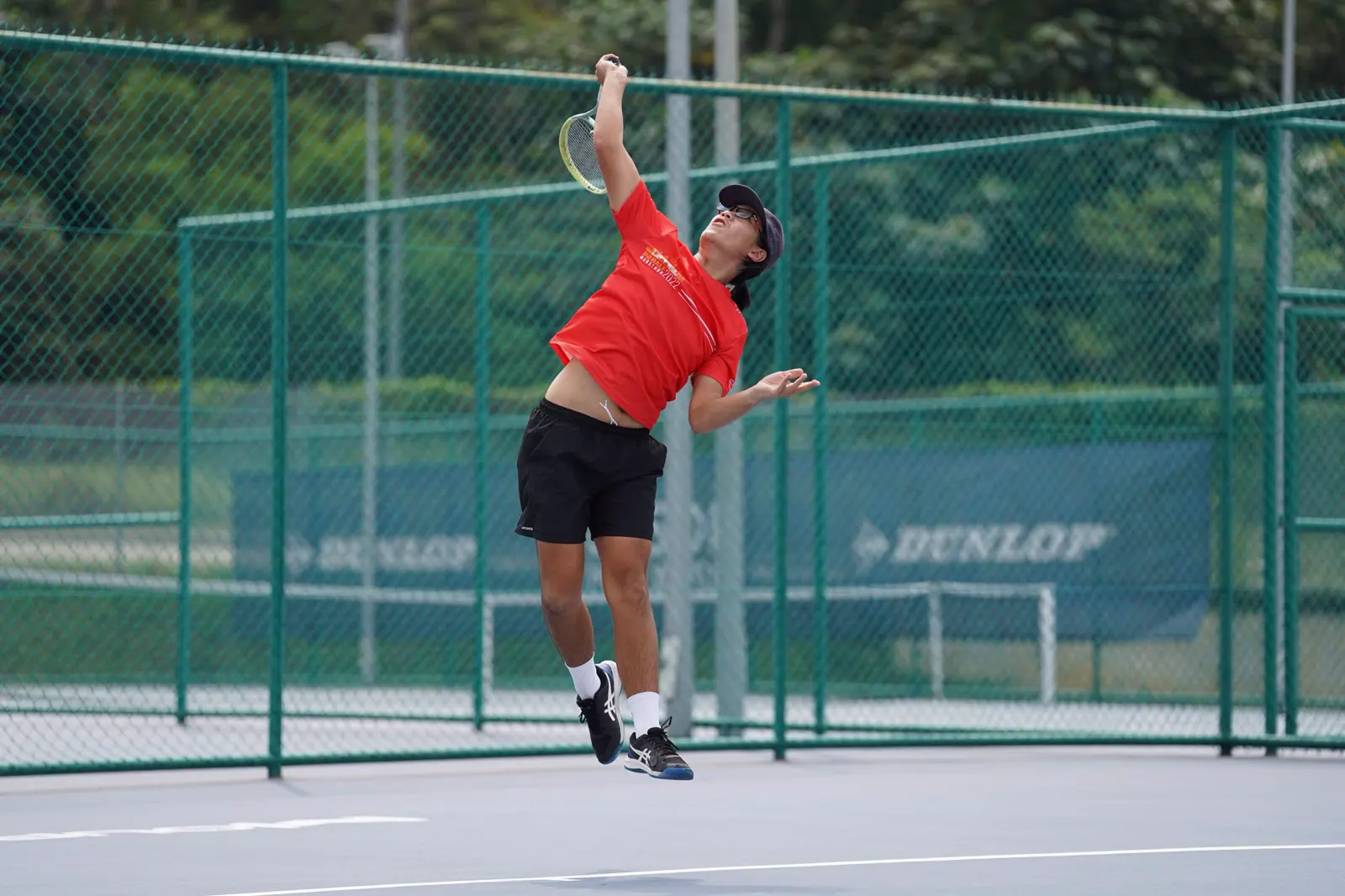 Spieler springt zu einem Schmetterball auf einem Tennisplatz im Freien