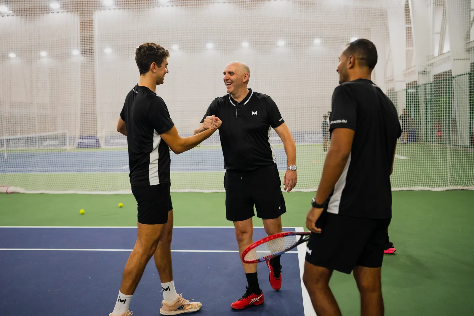Tennistrainer leitet zwei Spieler auf einem Platz im Freien an der Mouratoglou Academy Malaysia an