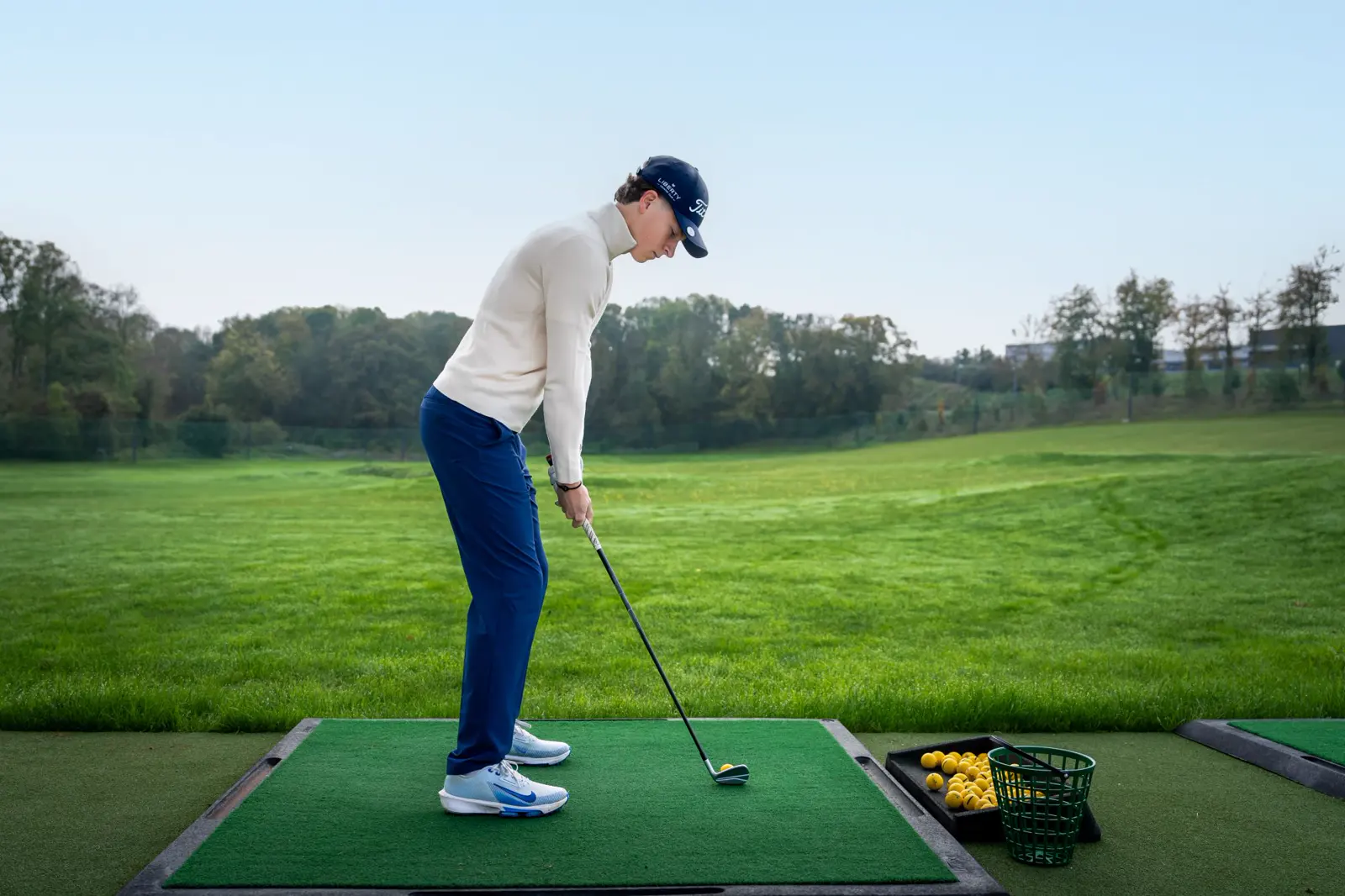 Golfista preparándose para golpear sobre una alfombra de prácticas en un campo de prácticas