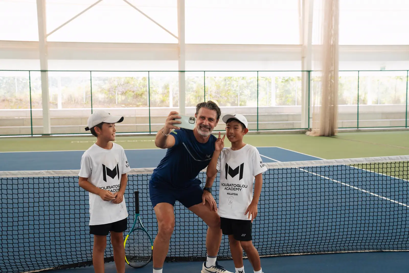 Patrick Mouratoglou haciéndose un selfi con alumnos en una pista cubierta de la Mouratoglou Academy Malaysia