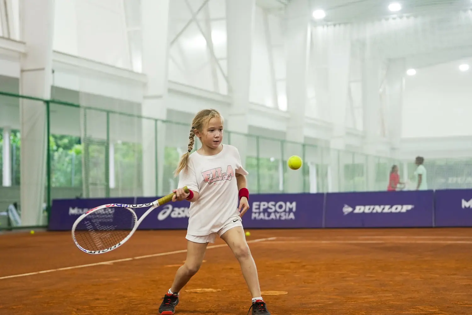Jeune fille frappant la balle sur un court couvert en terre battue à la Mouratoglou Academy Malaysia