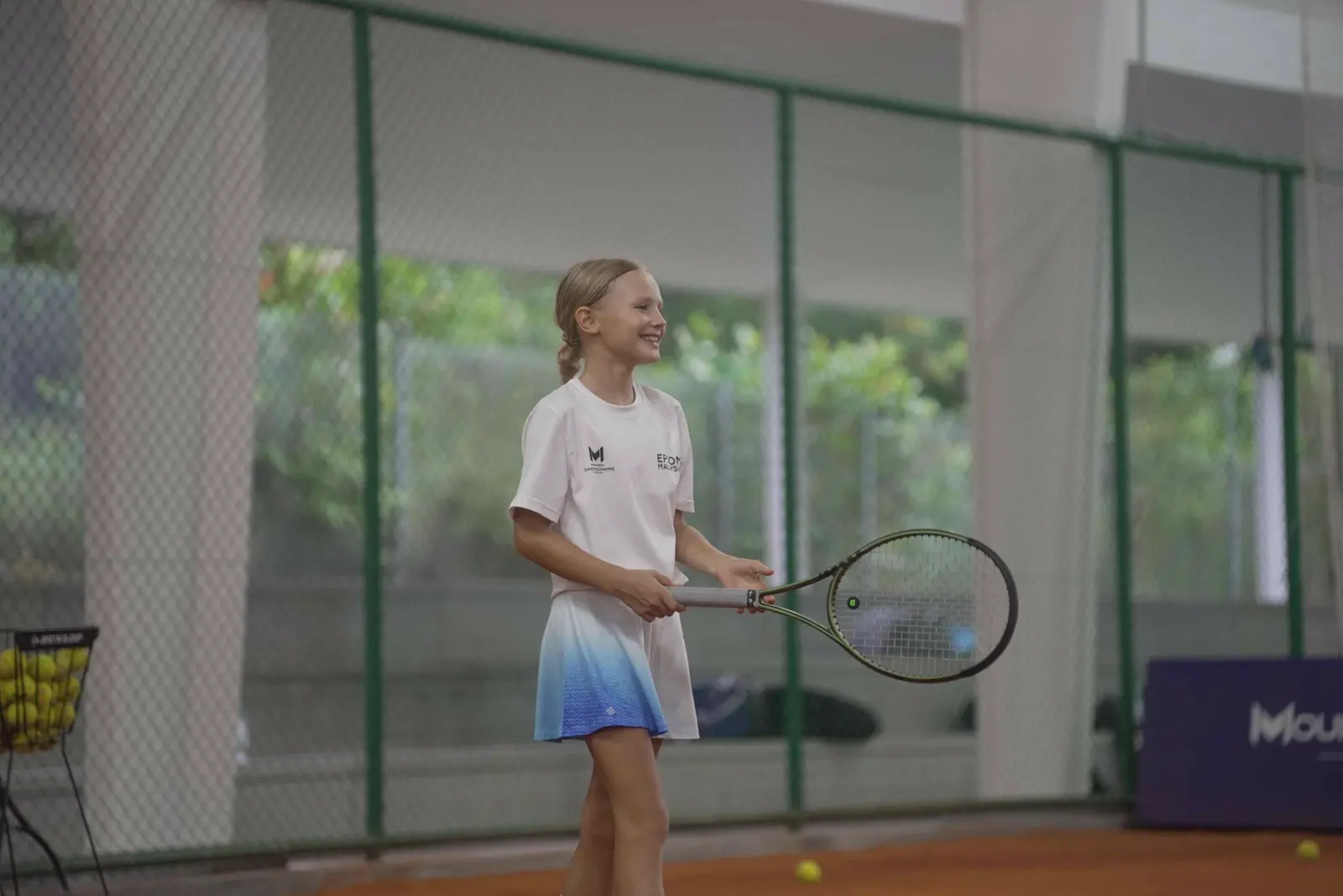 Jeune fille tenant une raquette de tennis sur un court couvert en terre battue à la Mouratoglou Academy Malaysia