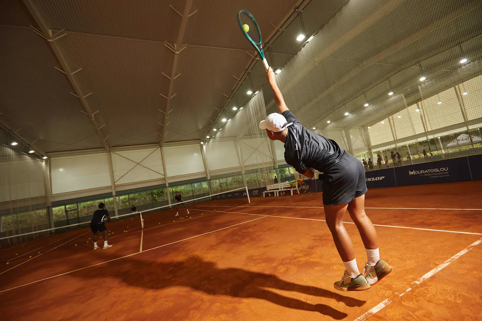 Schüler beim Aufschlag auf den überdachten Sandplätzen der Mouratoglou Academy Kuala Lumpur.