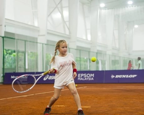 Junges Mädchen schlägt einen Ball auf einem Hallen-Sandplatz an der Mouratoglou Academy Malaysia auf dem Campus des Epsom College in Malaysia.