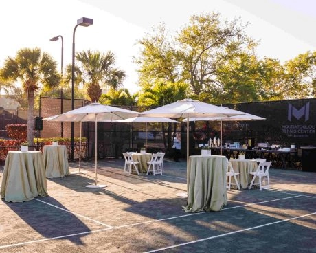 Empfangsbereich für ein Outdoor-Event auf den Plätzen des Mouratoglou Tennis Center Naples, Florida, mit Bewirtungsstationen und Sitzbereichen für Gäste.