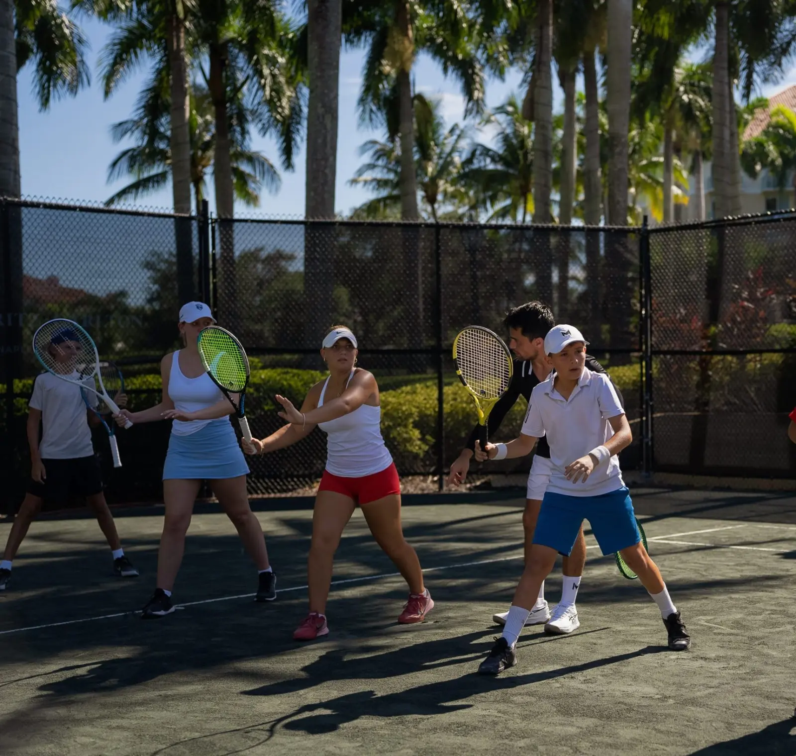 Tenistas adultos siguiendo las indicaciones de su entrenador en el Mouratoglou Tennis Center Naples