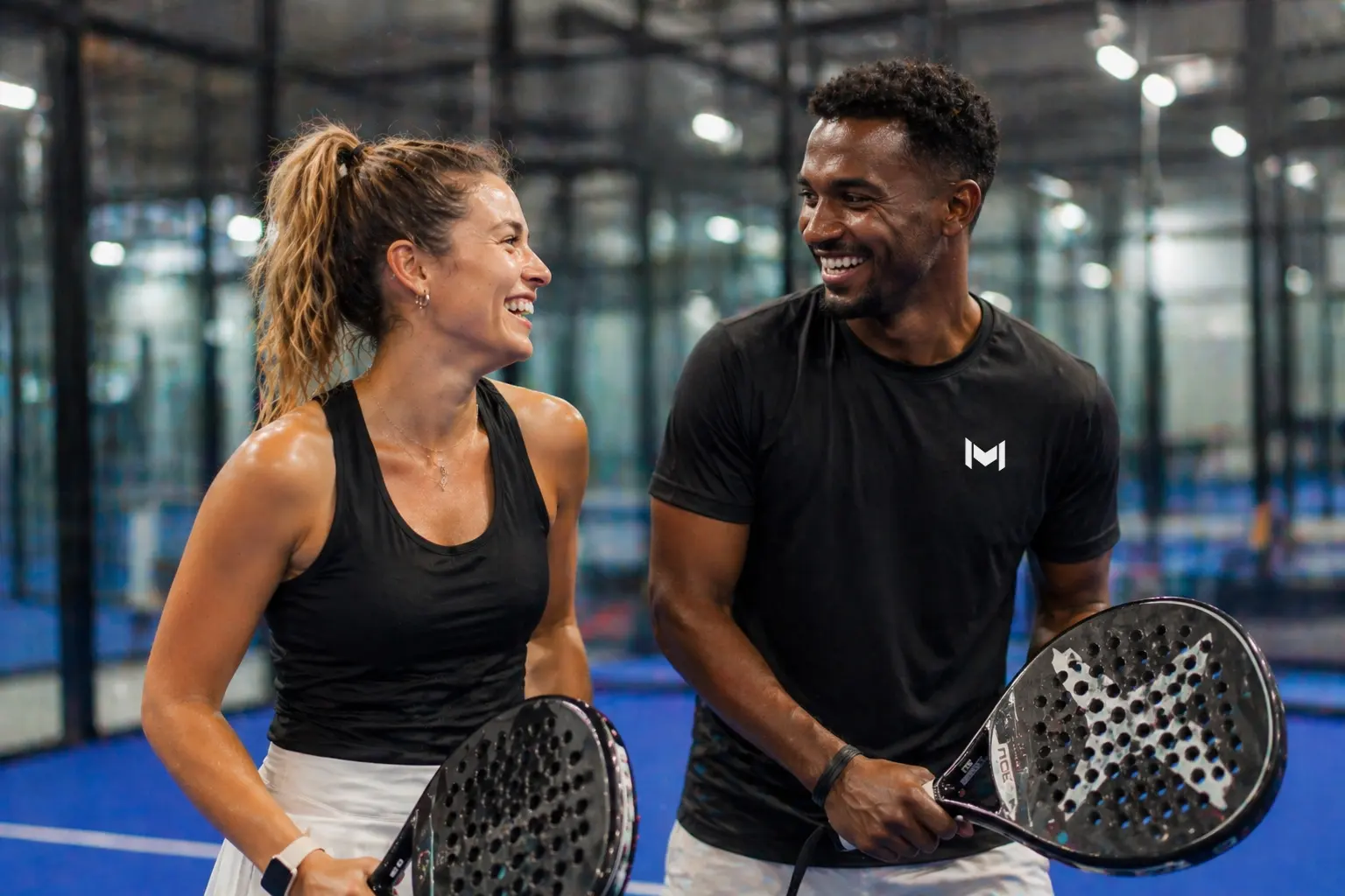 Dos jugadores de pádel sonriendo con sus palas en una pista cubierta