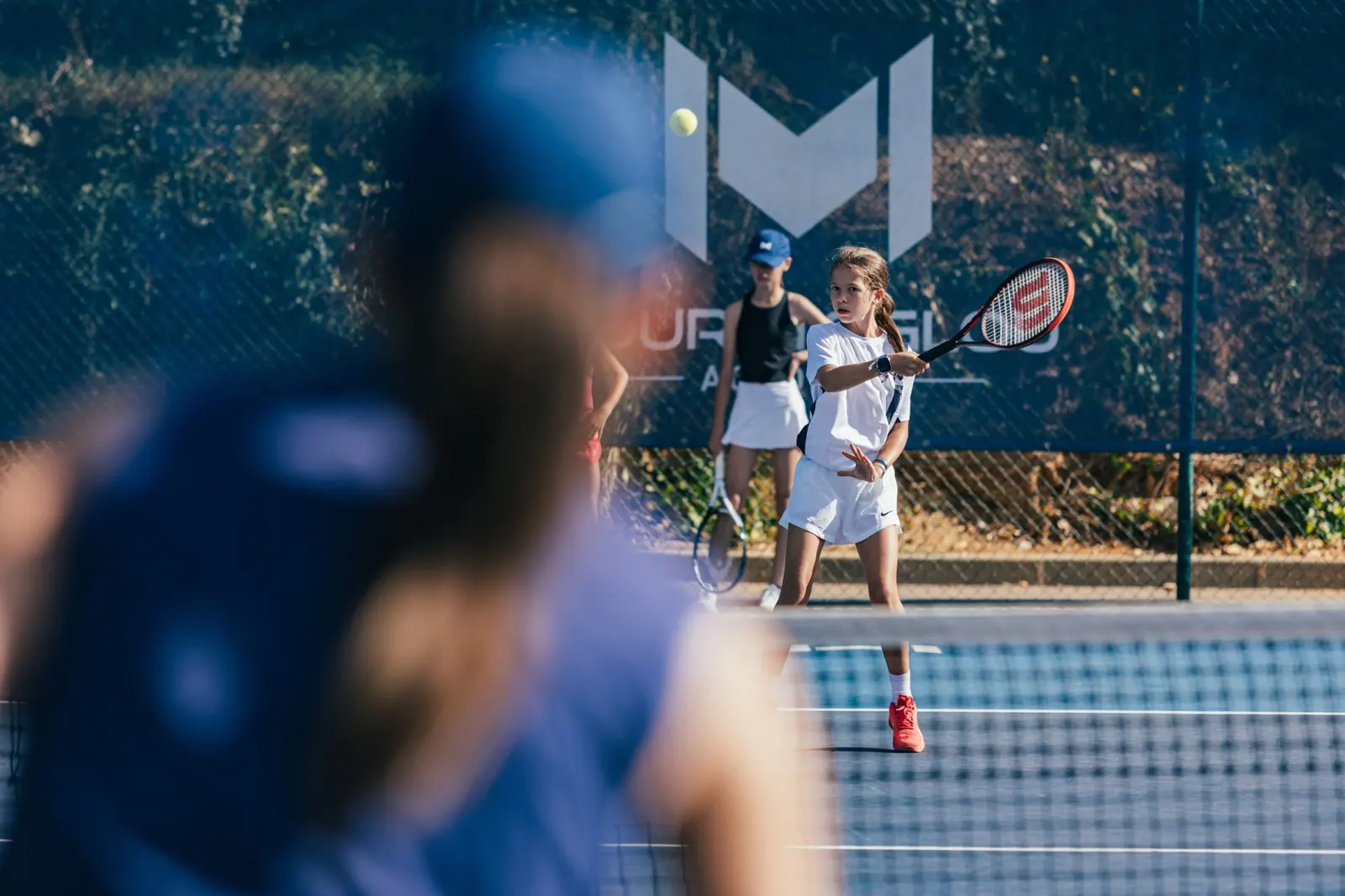 Entrenador hablando con jugadores junior en una pista exterior de tenis