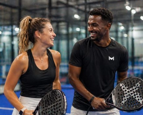 Dos jugadores de pádel sonrientes con sus palas en una pista cubierta.