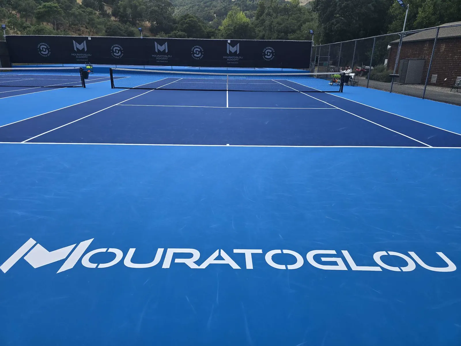 Blauer Tennisplatz mit dem Namen Mouratoglou und den Hügeln Kaliforniens an der Mouratoglou Academy San Francisco