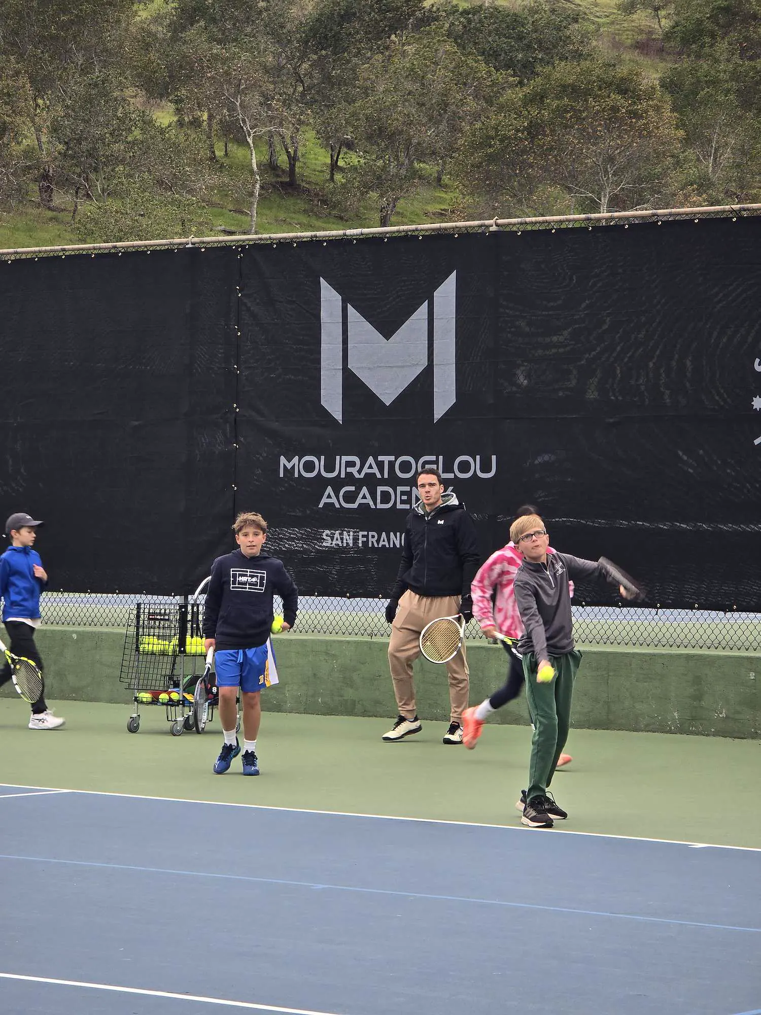 Junge Spieler mit ihrem Coach vor dem Banner der Mouratoglou Academy in San Francisco