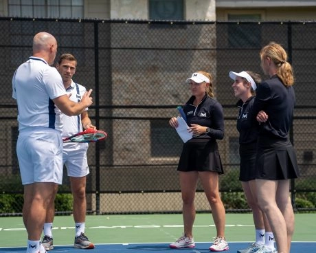 Cuatro jugadores participando en una clase de tenis con un entrenador en una pista exterior del Mouratoglou Tennis Center Horseshoe Bay.