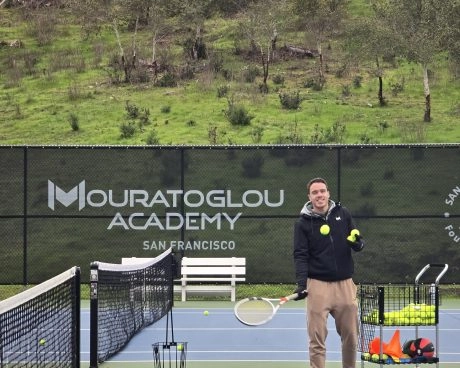 Entrenador de tenis lanzando pelotas a los jugadores en una pista exterior de la Mouratoglou Academy San Francisco.