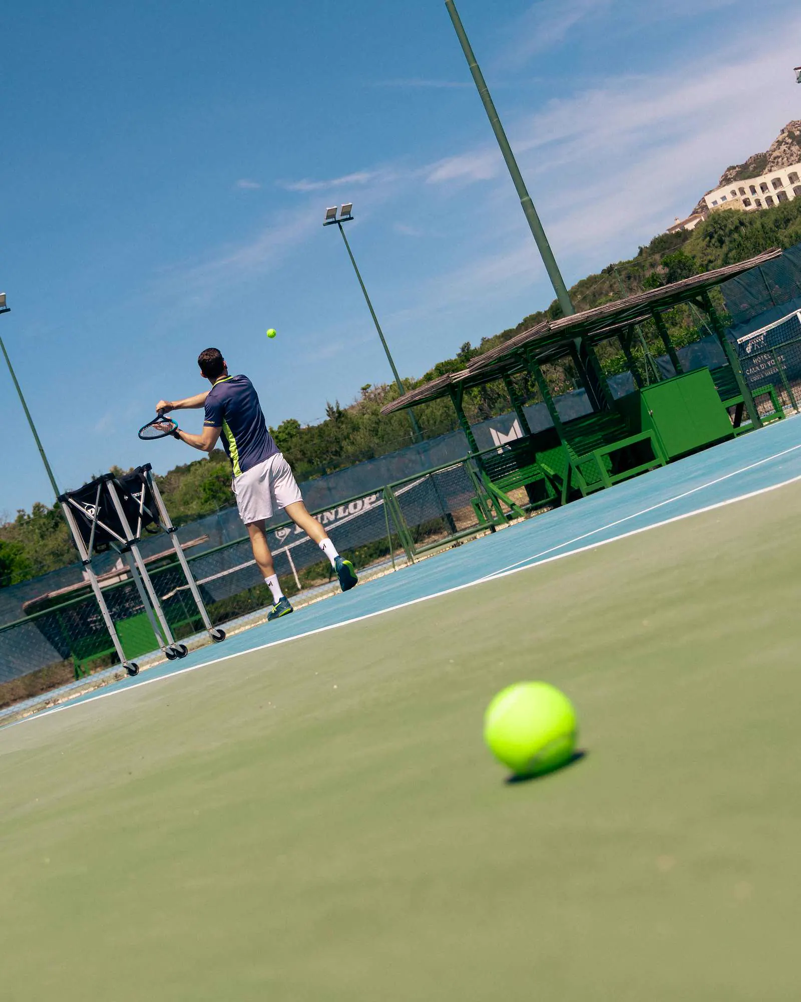 Spieler beim Aufschlag, mit einem Tennisball im Vordergrund, in Cala di Volpe, Sardinien.