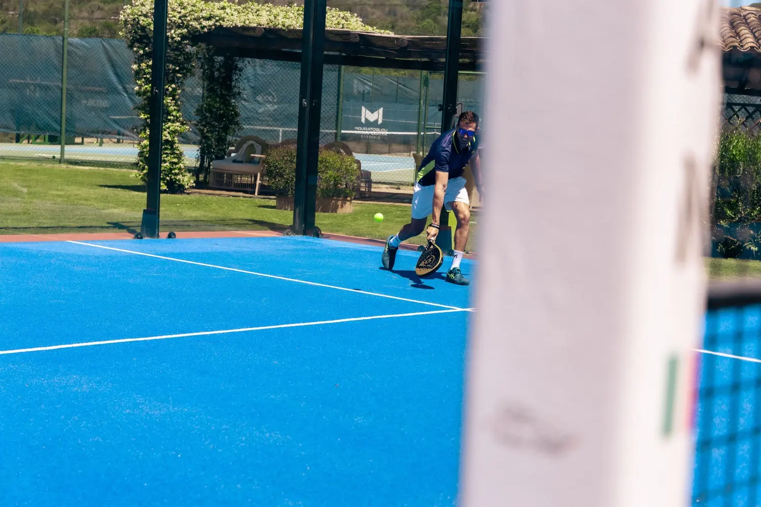 Joueur de padel se déplaçant vers la balle sur un court bleu à Cala di Volpe