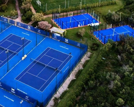 Luftaufnahme der Padel- und Tennisplätze im Freien bei M Padel Sardinia, umgeben von gepflegtem Grün und erstklassigen Sportanlagen.