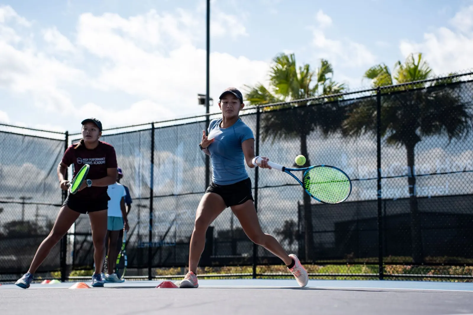 Dos jóvenes jugadores practicando un ejercicio de derecha en una pista exterior