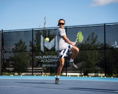Jeune joueur de tennis sautant pour frapper un coup droit à l’entraînement