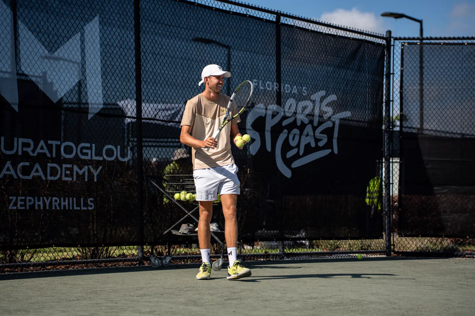 Coach de tennis tenant des balles et une raquette sur le court à la Mouratoglou Academy Zephyrhills