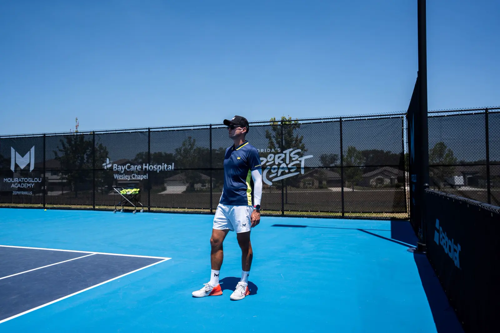 Entrenador de tenis dando indicaciones a jugadores en una pista soleada de la Mouratoglou Academy Zephyrhills