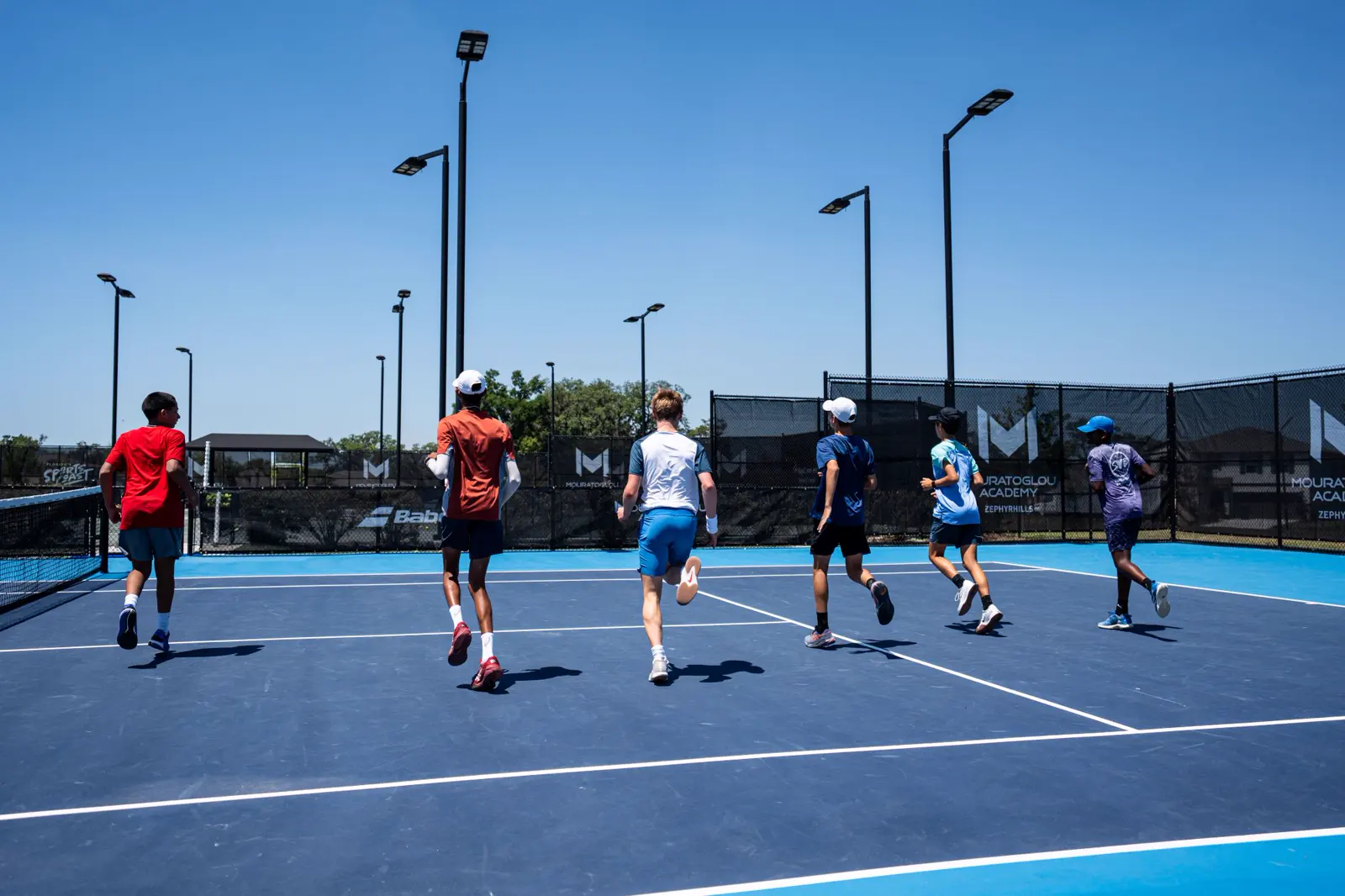 Giovani tennisti fanno corsa di riscaldamento su un campo blu alla Mouratoglou Academy Zephyrhills
