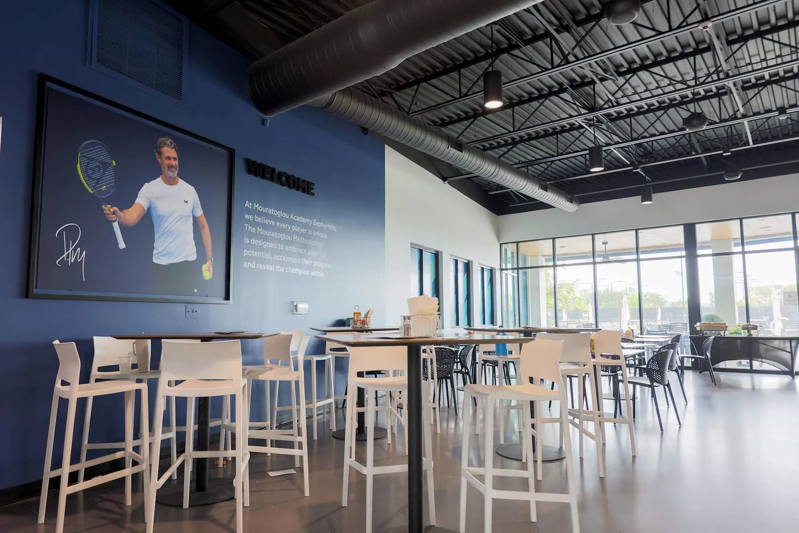 Spieler-Lounge mit Stehtischen und Bildschirmen an der Mouratoglou Academy Zephyrhills.