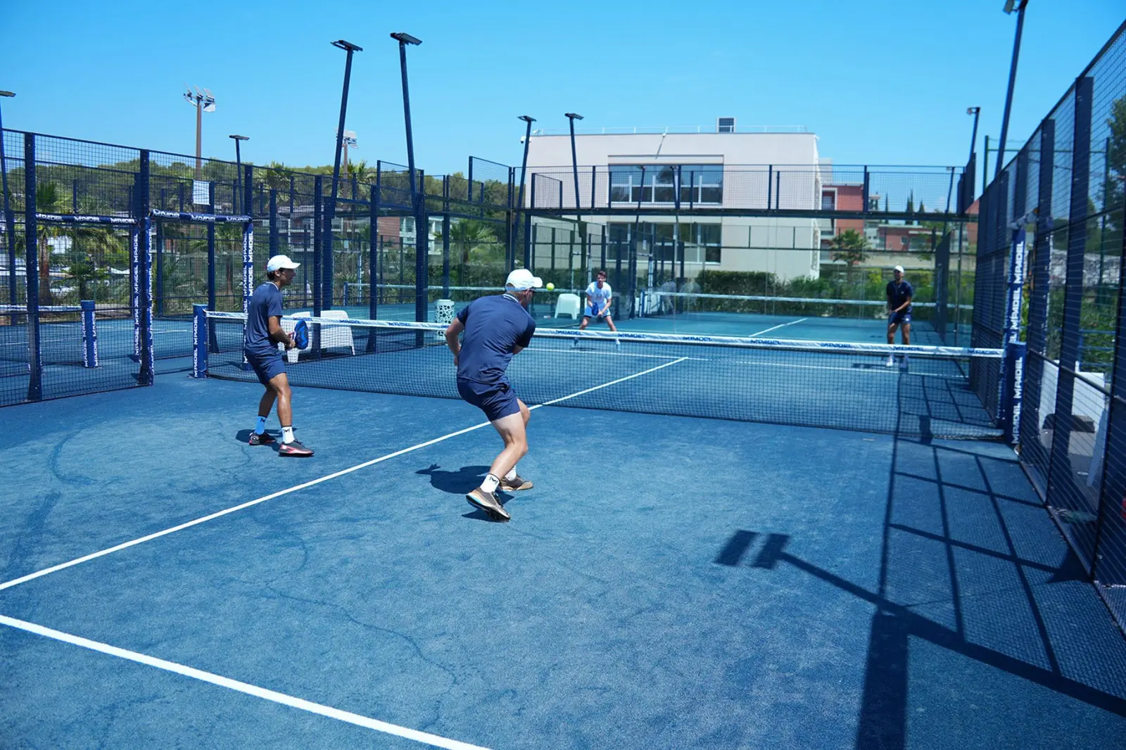 Vier Spieler bei einer Padel-Gruppenstunde mit einem Coach auf einem Außenplatz