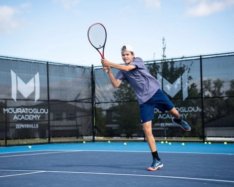 Tennisspieler schlägt eine Vorhand während einer Outdoor-Trainingseinheit mit einem Coach auf dem Platz
