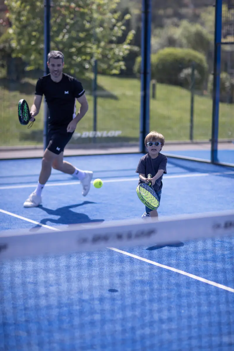 Père et fils jouant au padel sur un court bleu