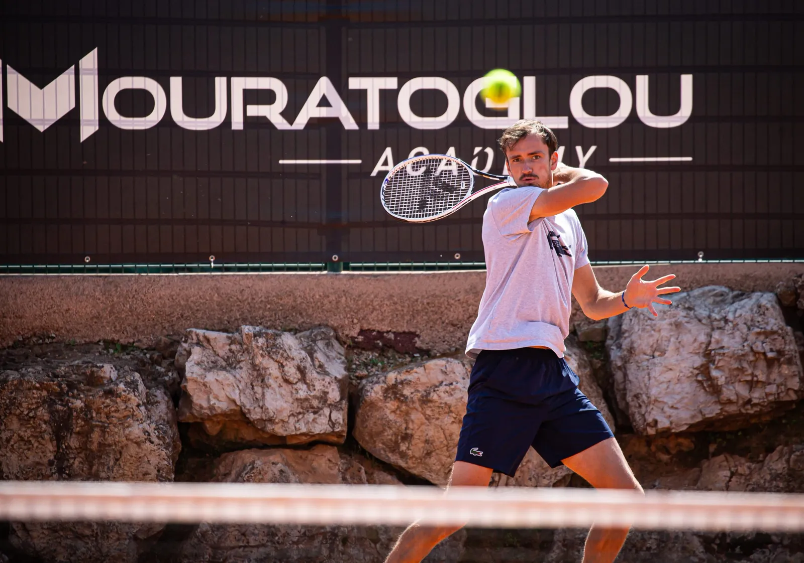 Daniil Medvedev schlägt eine Vorhand auf Sand vor dem Banner der Mouratoglou Academy