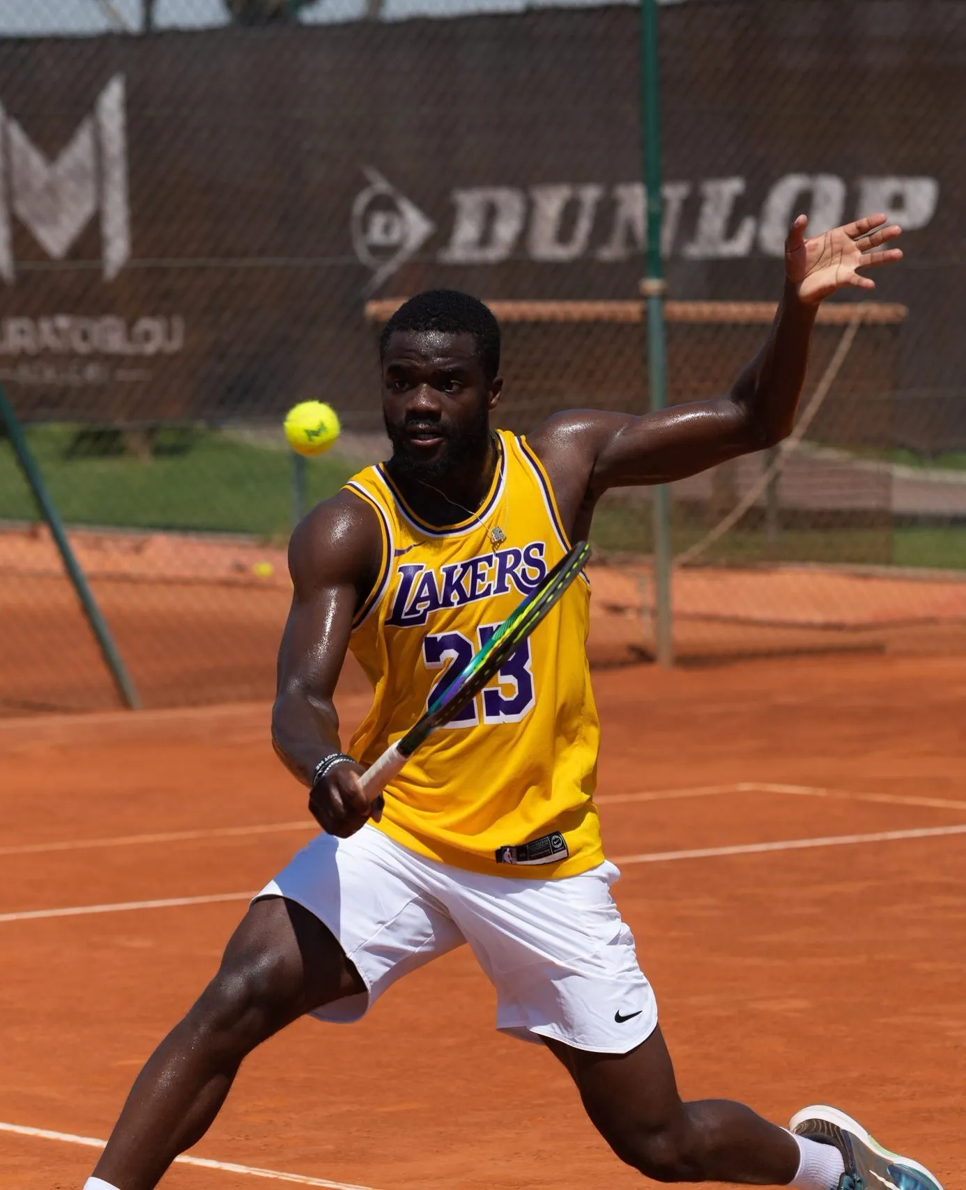 Frances Tiafoe im Basketballtrikot schlägt eine Rückhand auf Sand an der Akademie