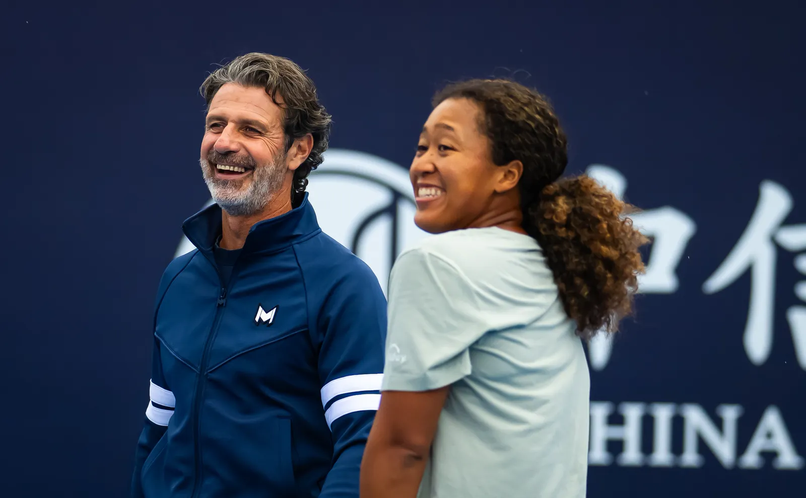 Naomi Osaka and Patrick Mouratoglou smiling together courtside