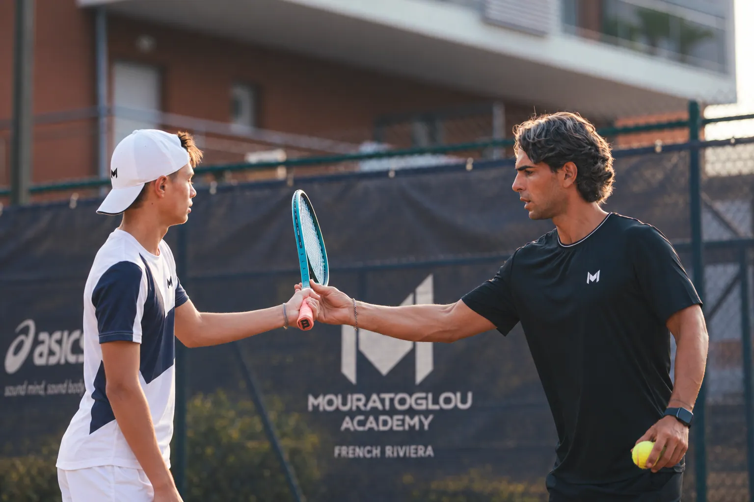 Coach in a black Mouratoglou T-shirt with a young player on court