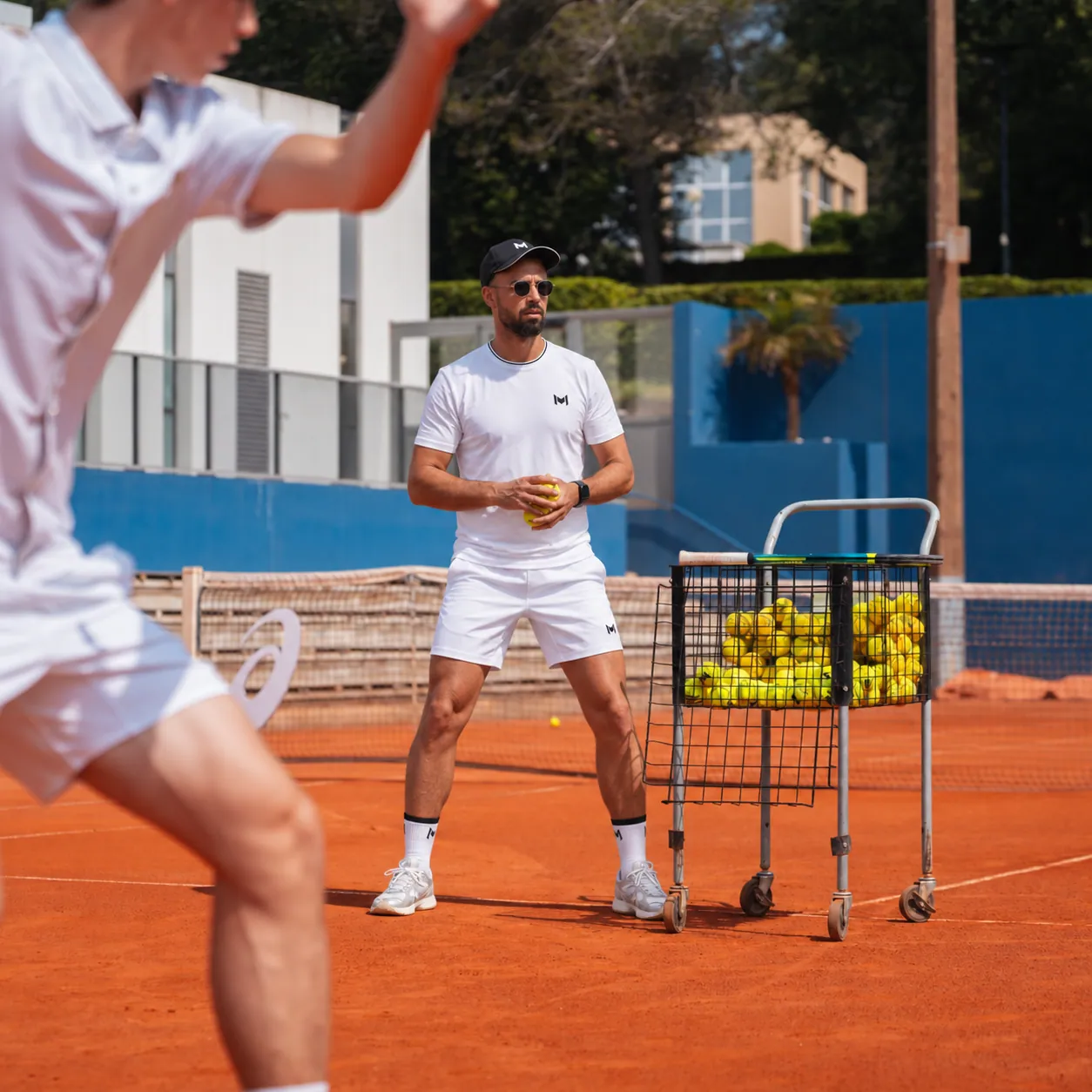 Coach donnant des balles à un stagiaire adulte sur terre battue pendant un stage de Pâques à la Mouratoglou Academy